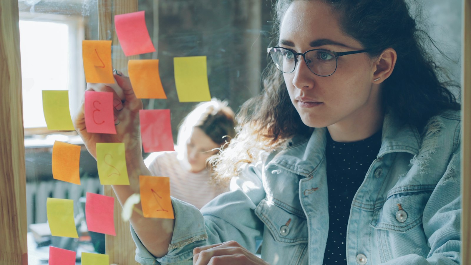 A woman arranging sticky notes on a glass wall during a workshop