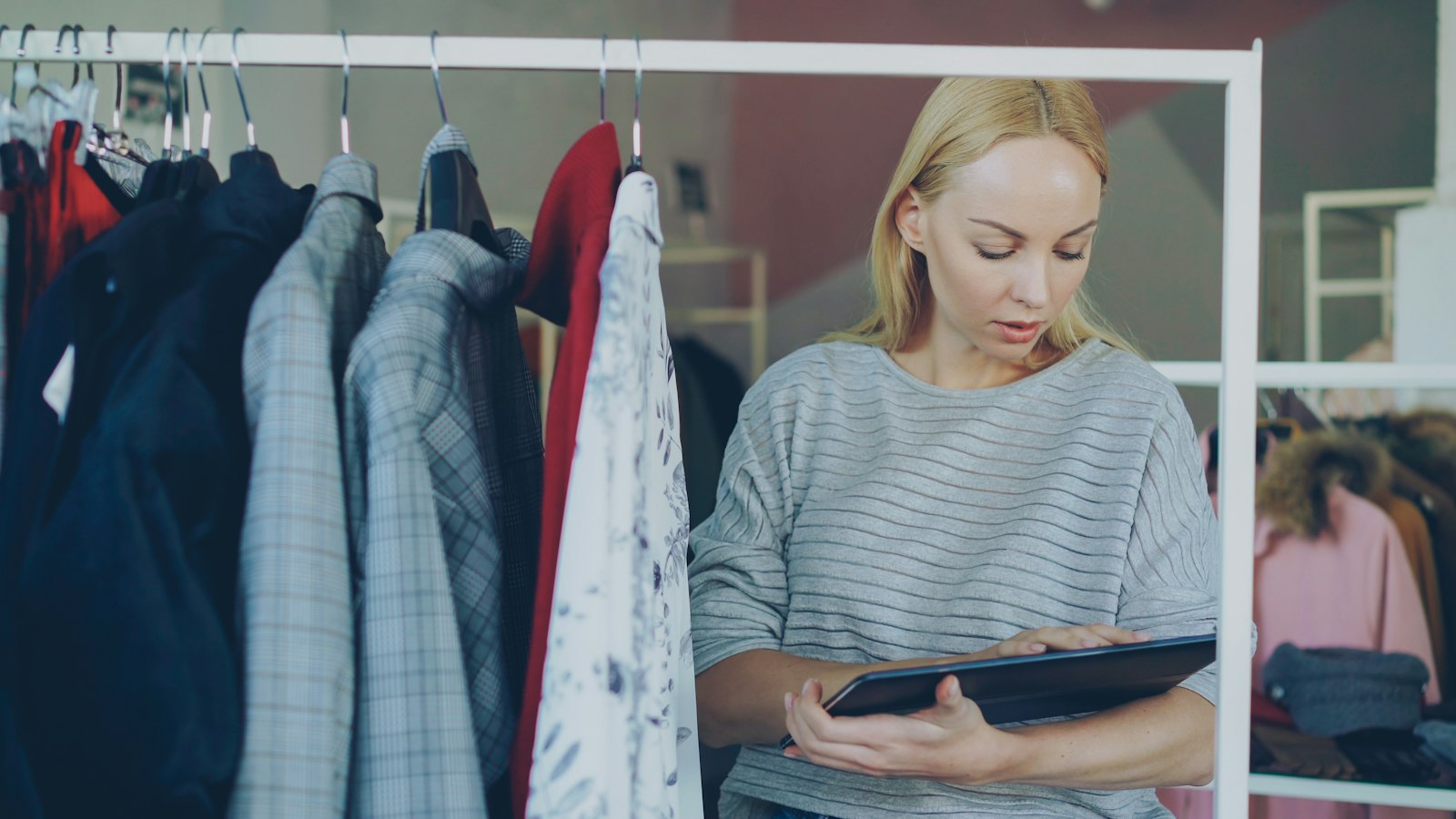 A boutique owner checking stock on a tablet between rails