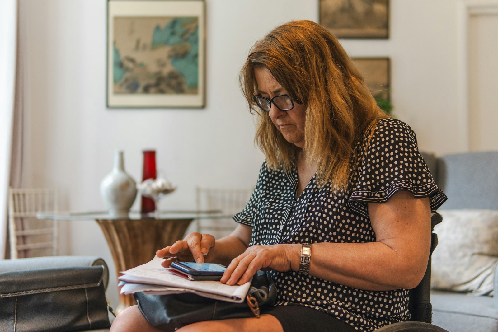 A woman at home checking her phone with papers on her lap