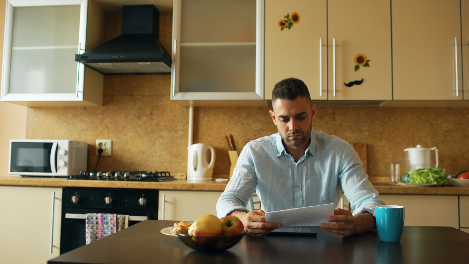 A man reading a document at a kitchen table with a cup of coffee