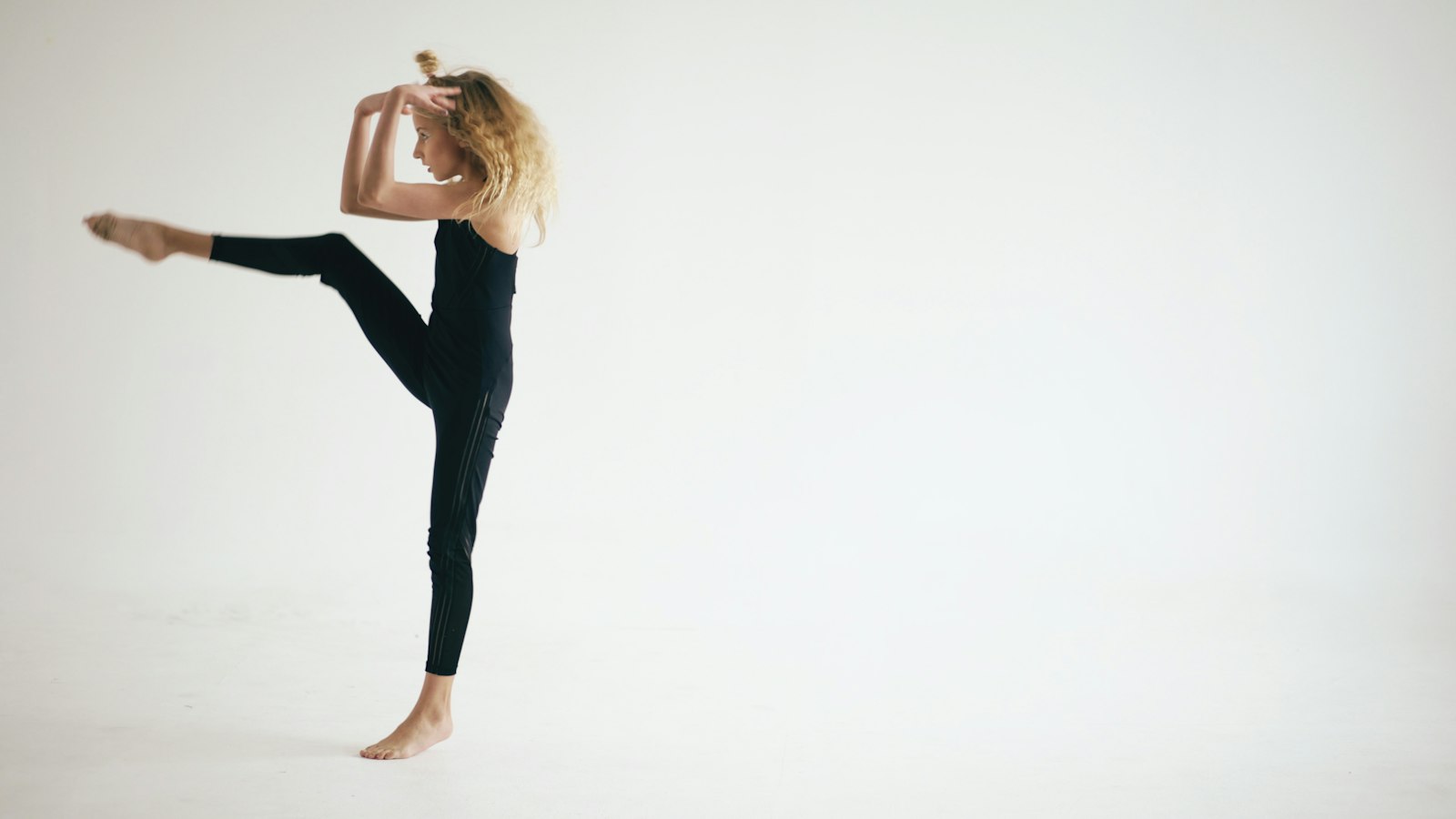 A young dancer in a black leotard with one leg raised