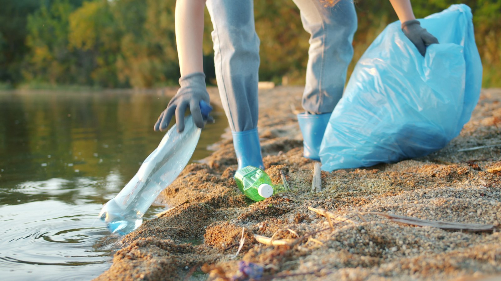 A gloved hand picking a plastic bottle from the water