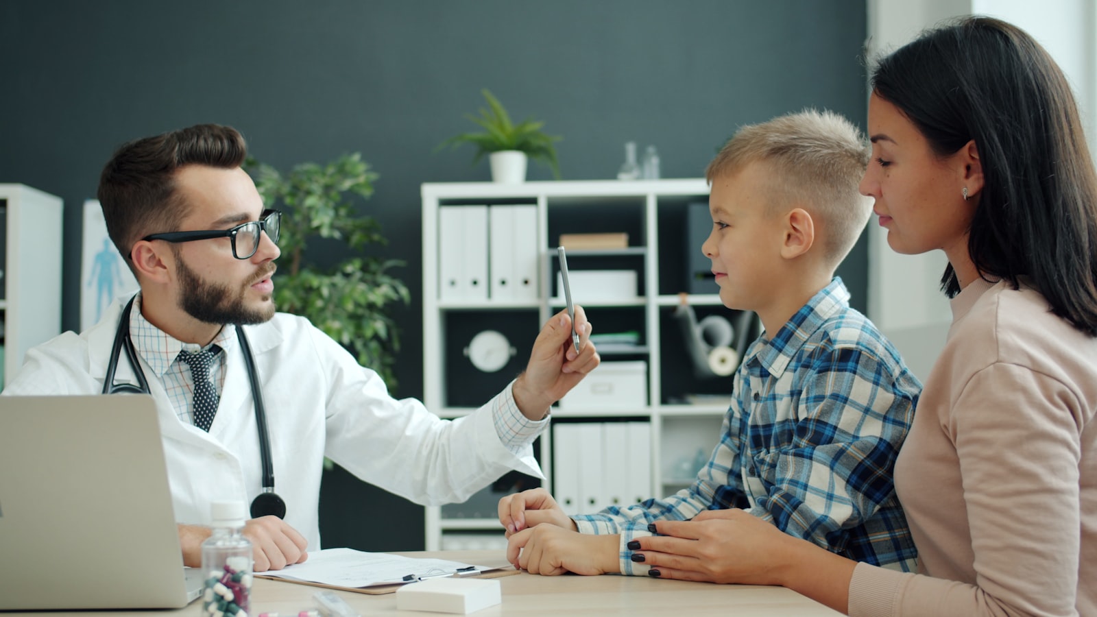 A doctor examining a boy while his mother watches