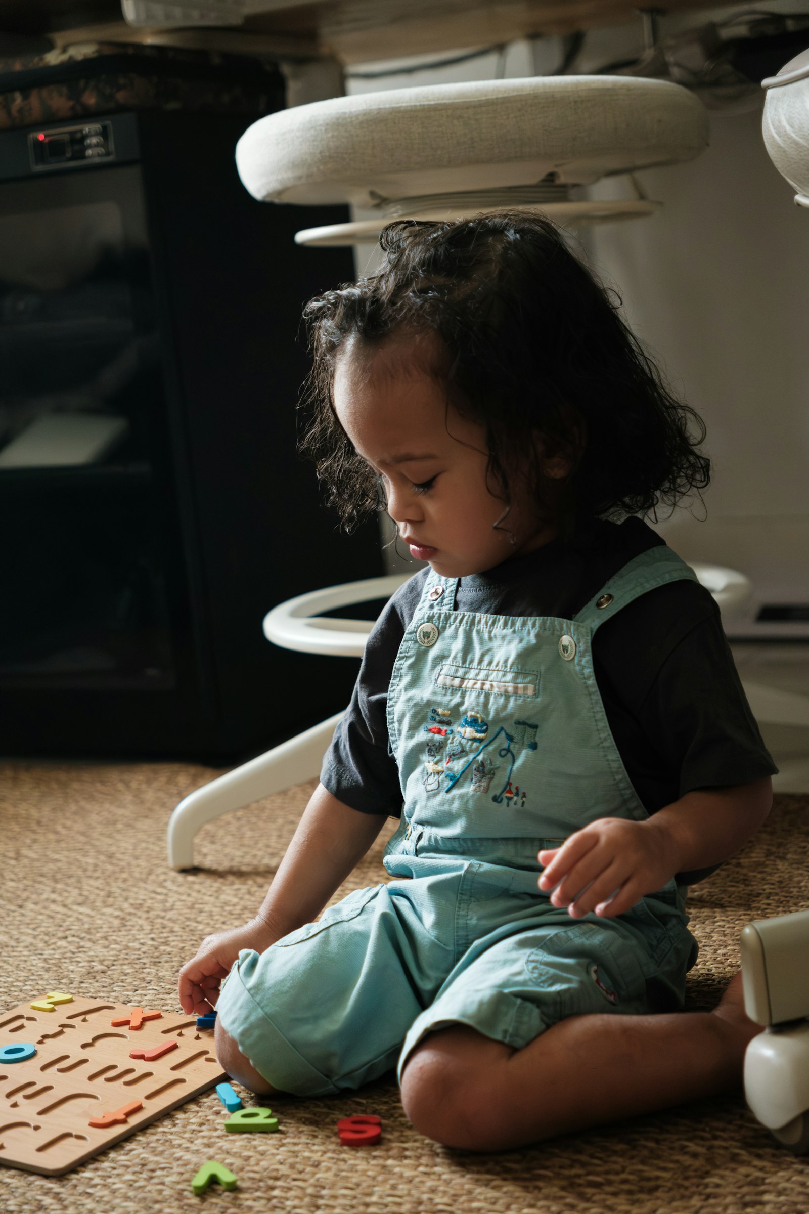 A young child in dungarees absorbed in a floor puzzle