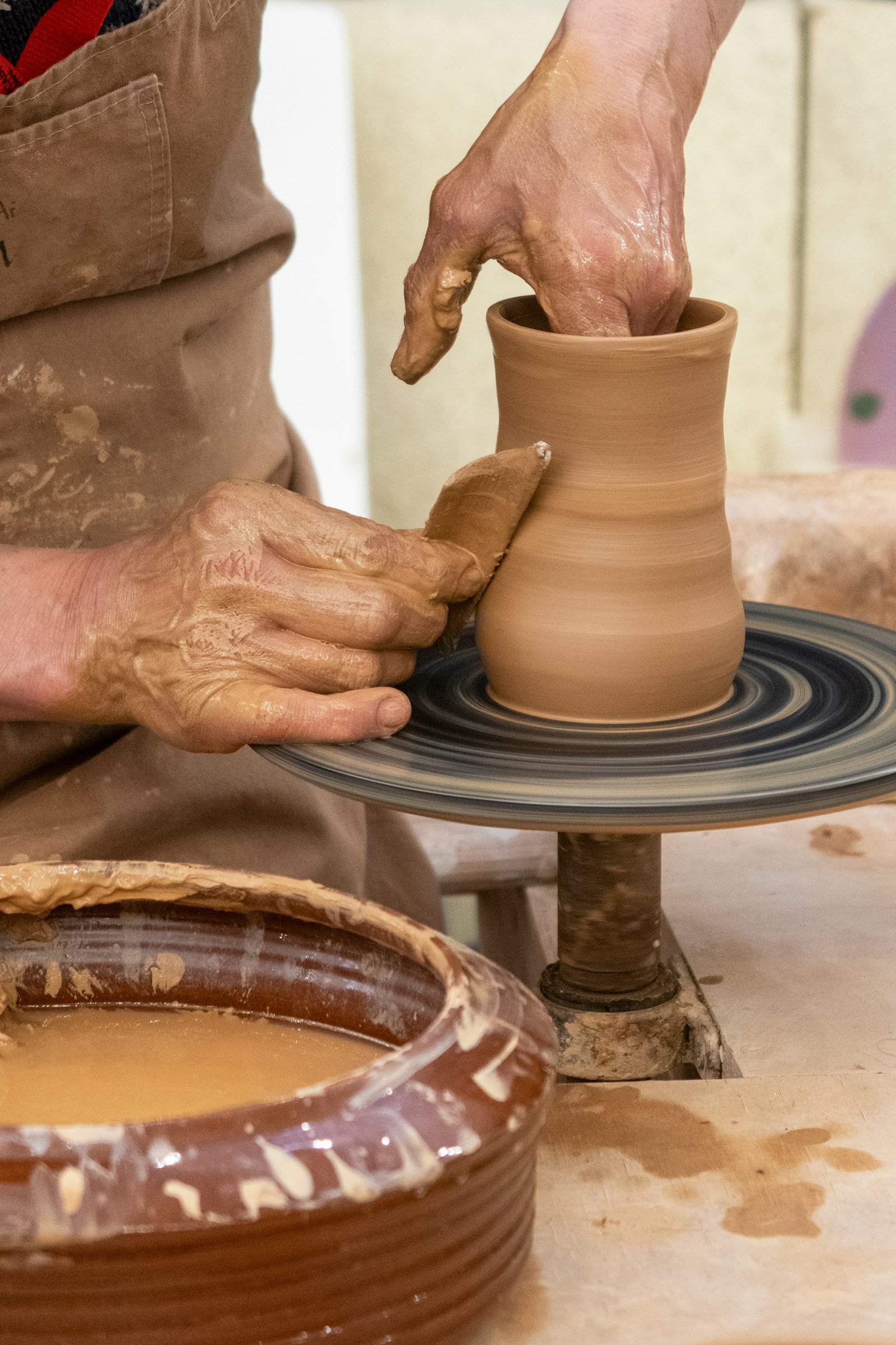 Clay-covered hands raising a vase on the wheel