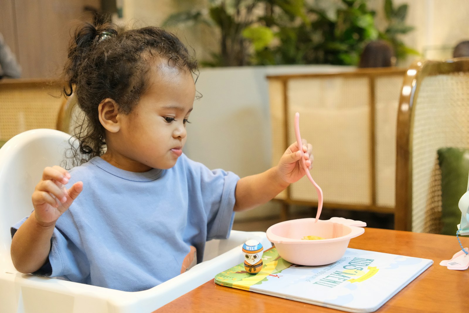 A young child eating from a bowl with a pink spoon