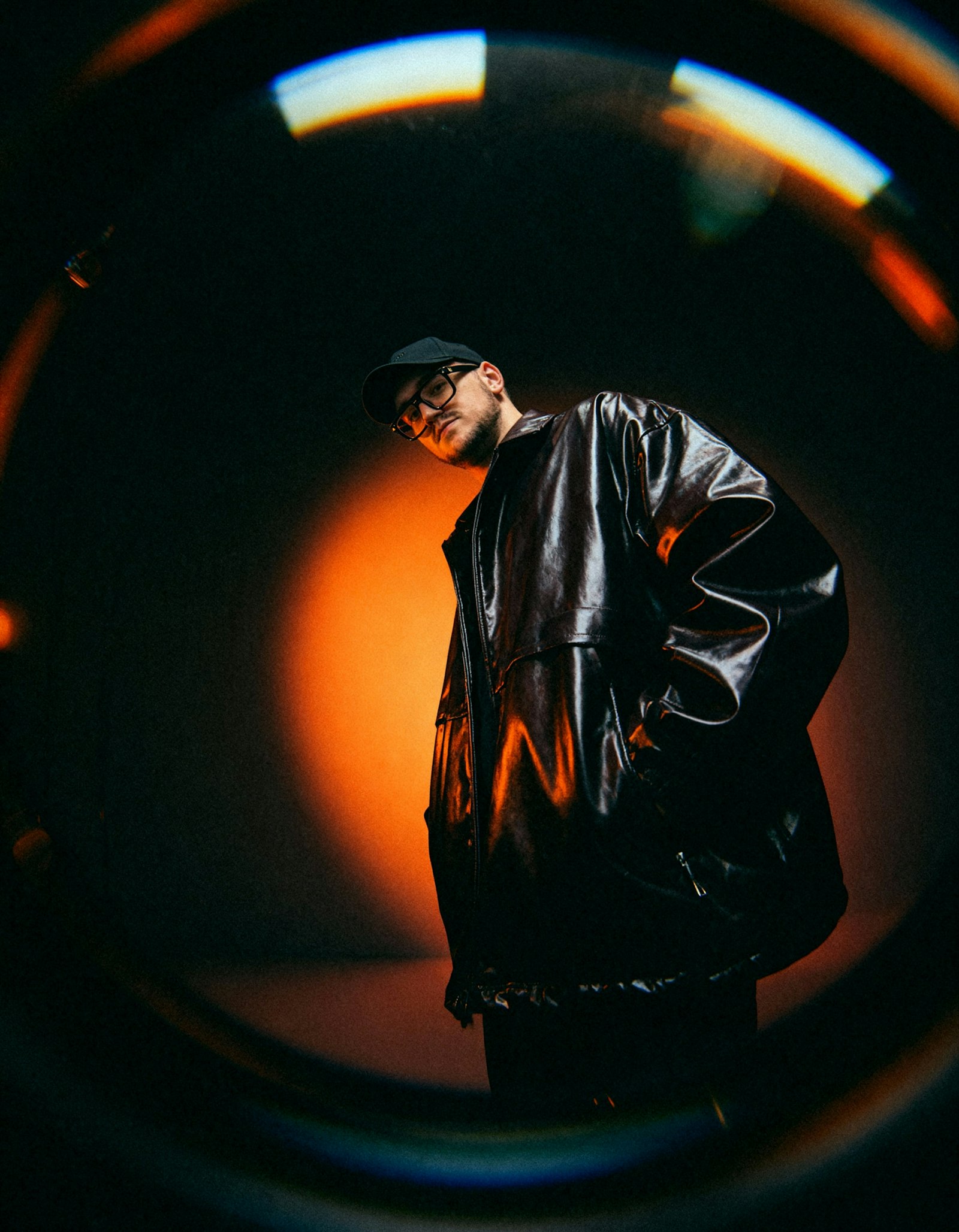 Alex Rivers in a leather jacket and cap under a ring of warm light