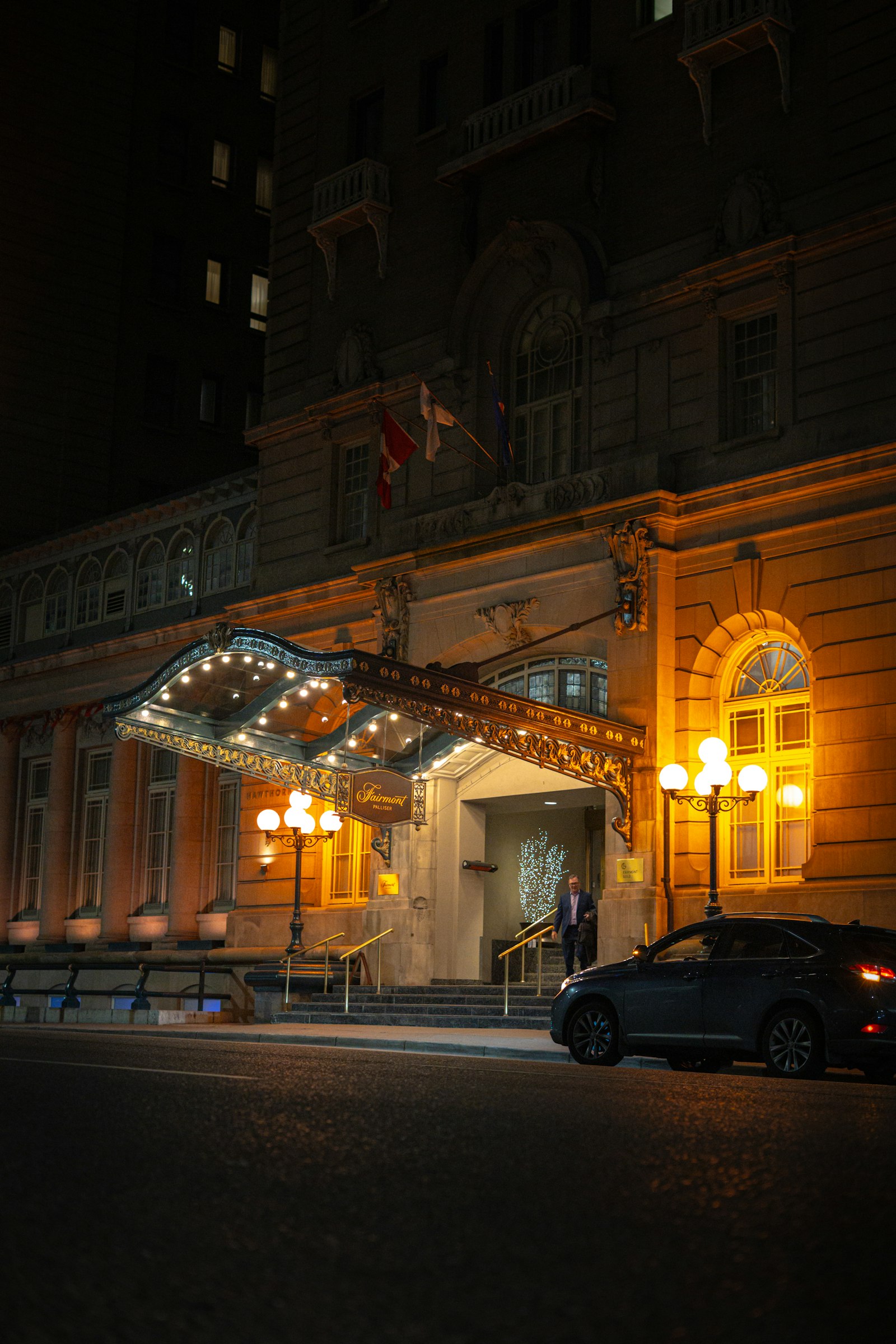 A grand hotel entrance at night with a dark car waiting outside