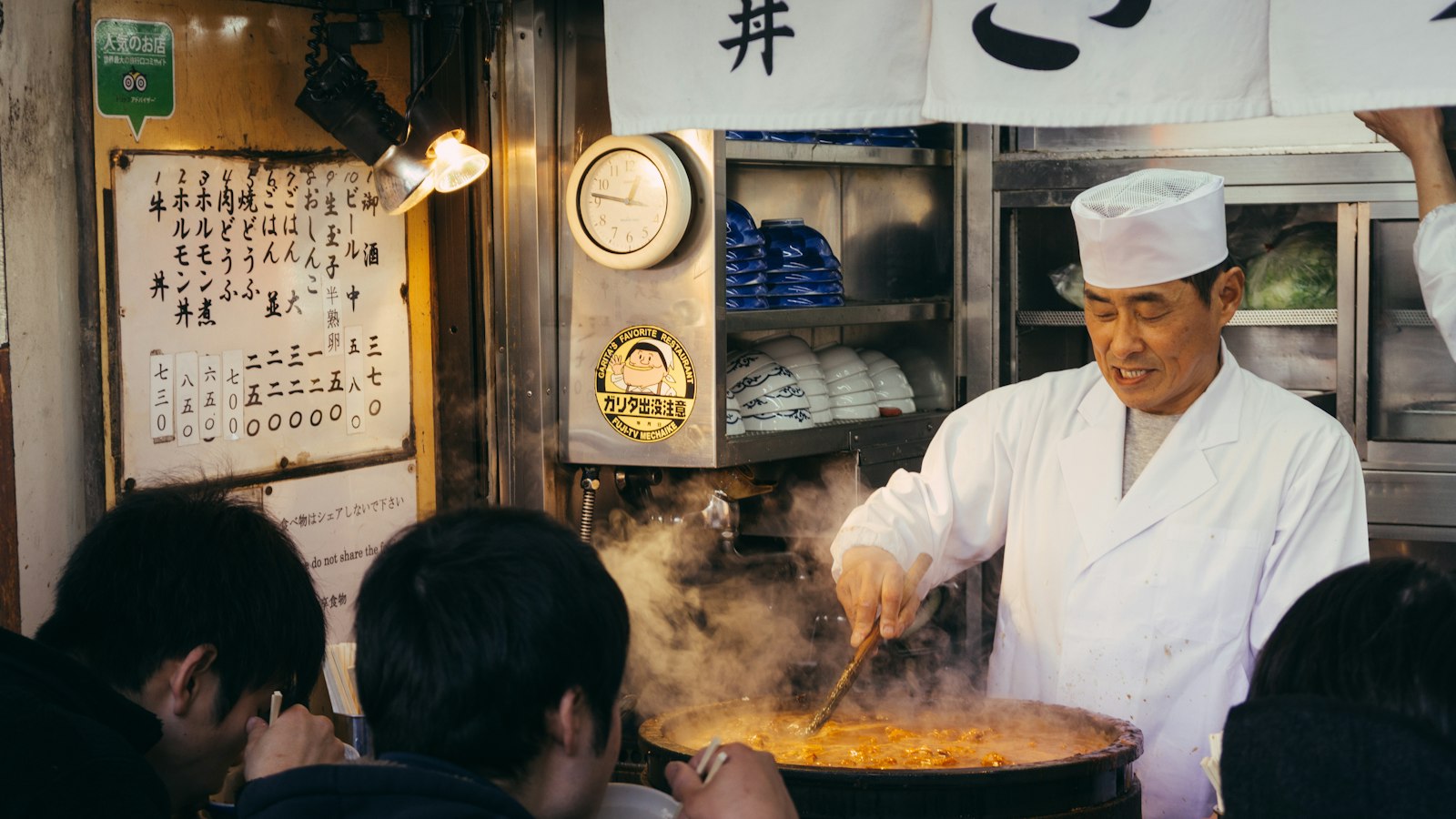 A cook stirring a steaming pot at a small counter