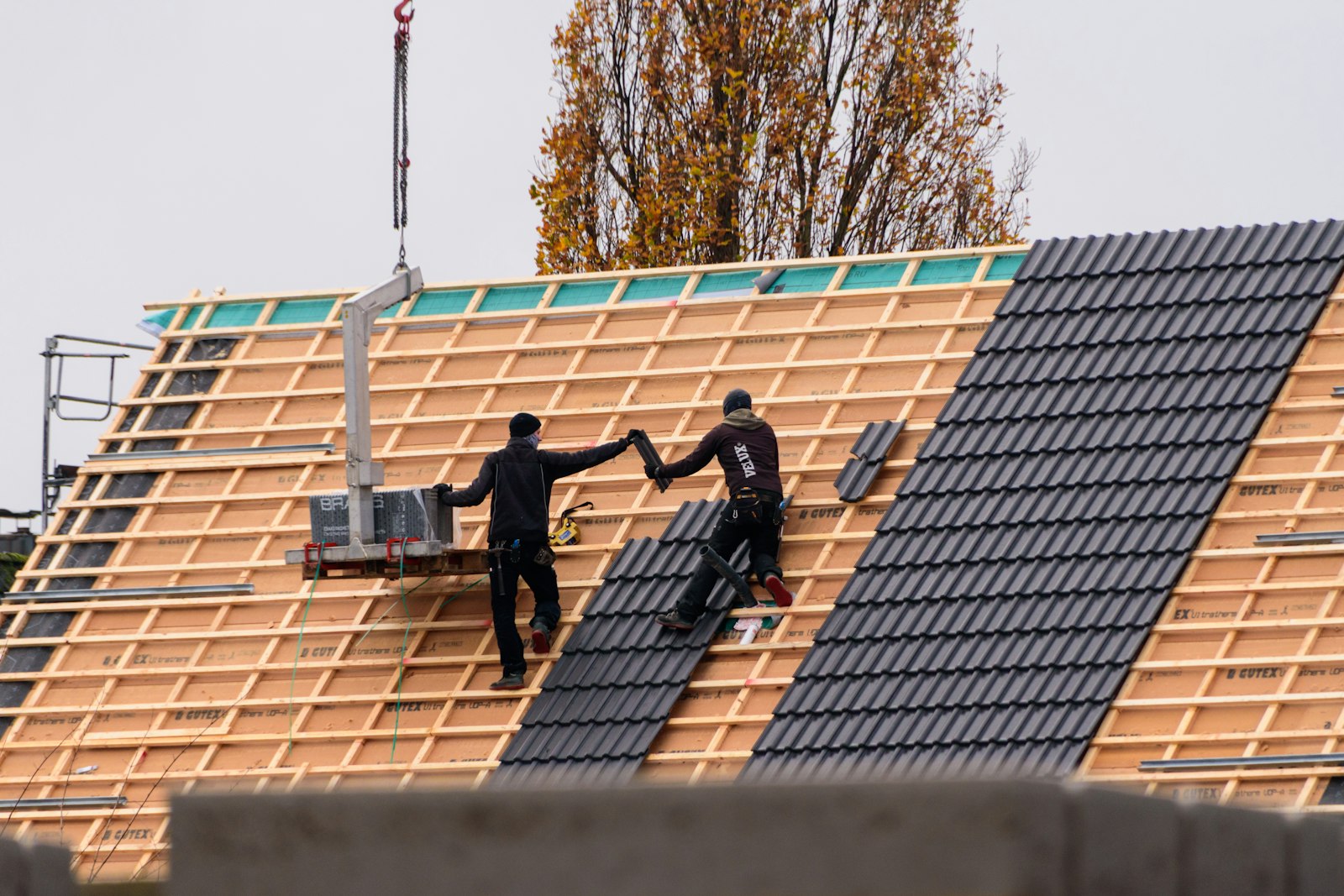 Two roofers laying dark tiles onto the timber battens of a new roof