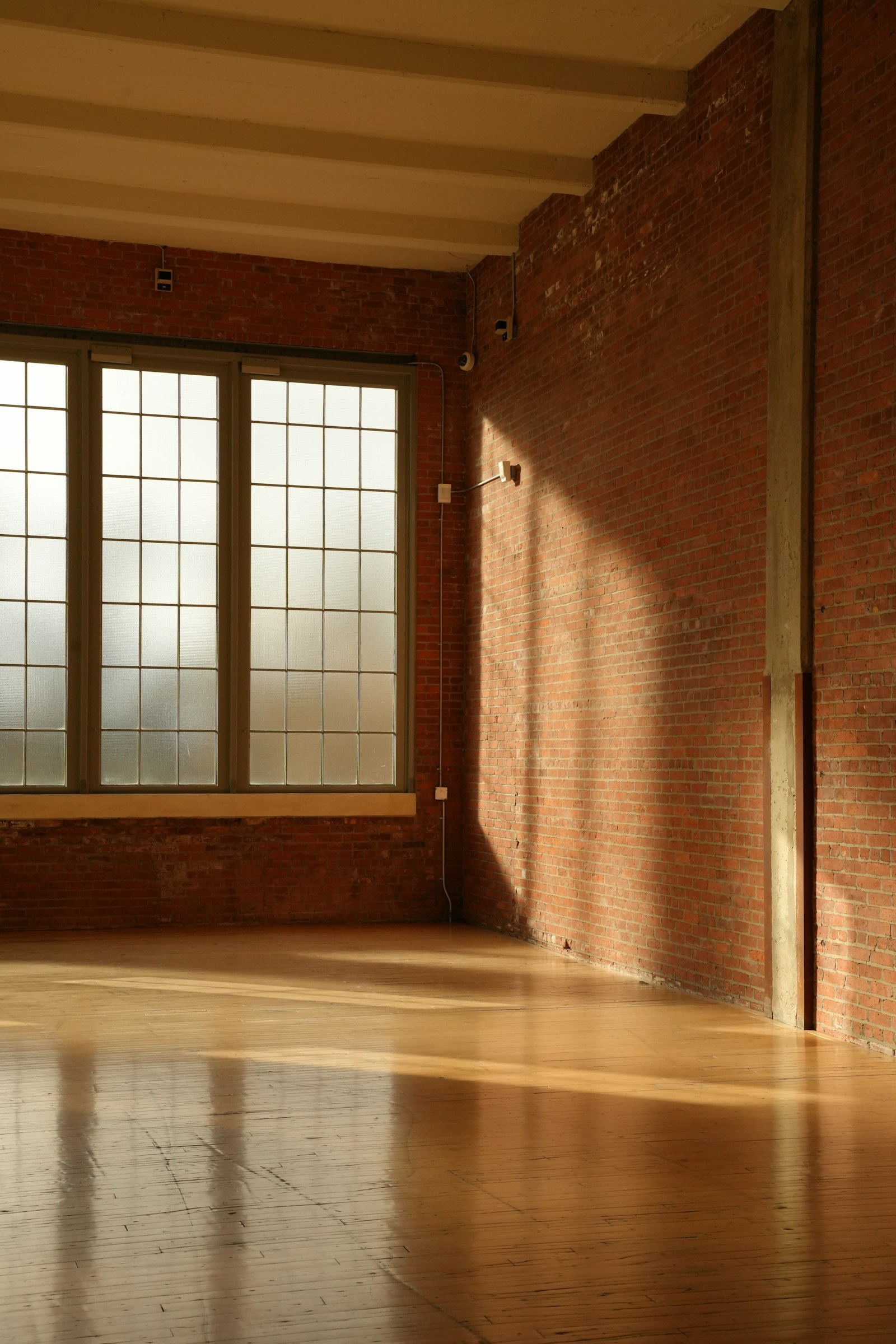 Sunlight across an empty wooden floor beside a brick wall