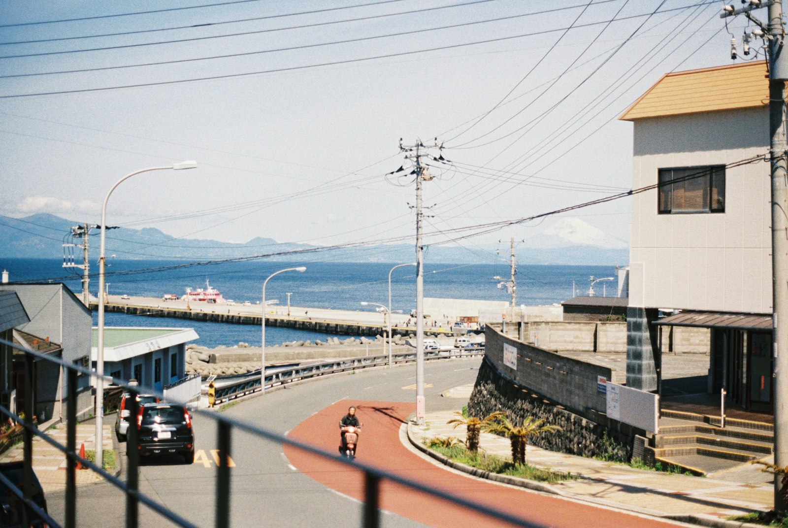 A coast road curving down to a harbour town with mountains behind