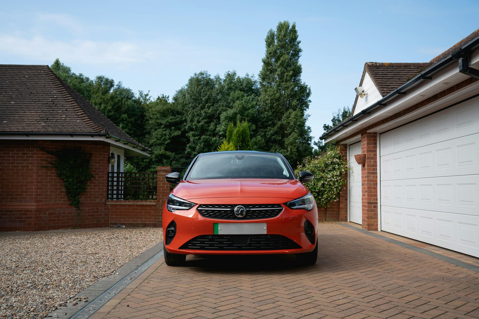 An orange hatchback parked on a block-paved drive