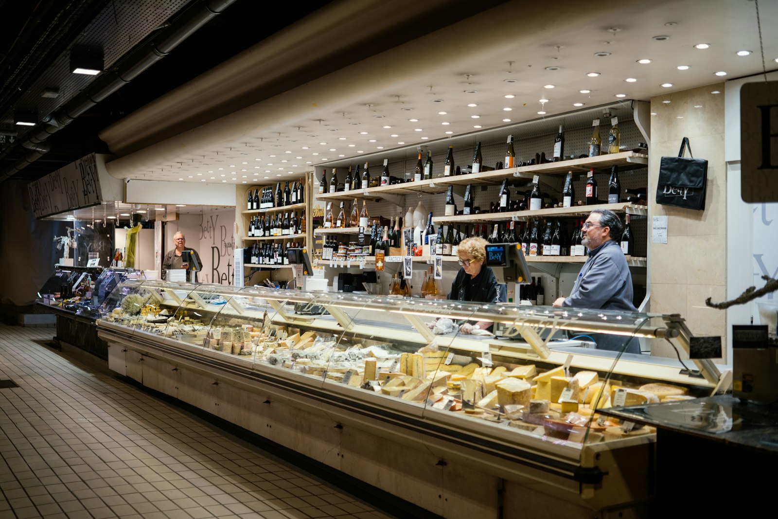 A long cheese and deli counter with wine shelves behind