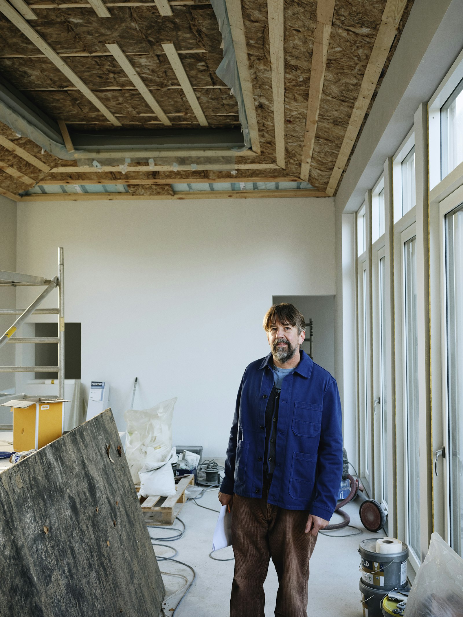 A builder standing in a room mid-renovation with the ceiling joists exposed