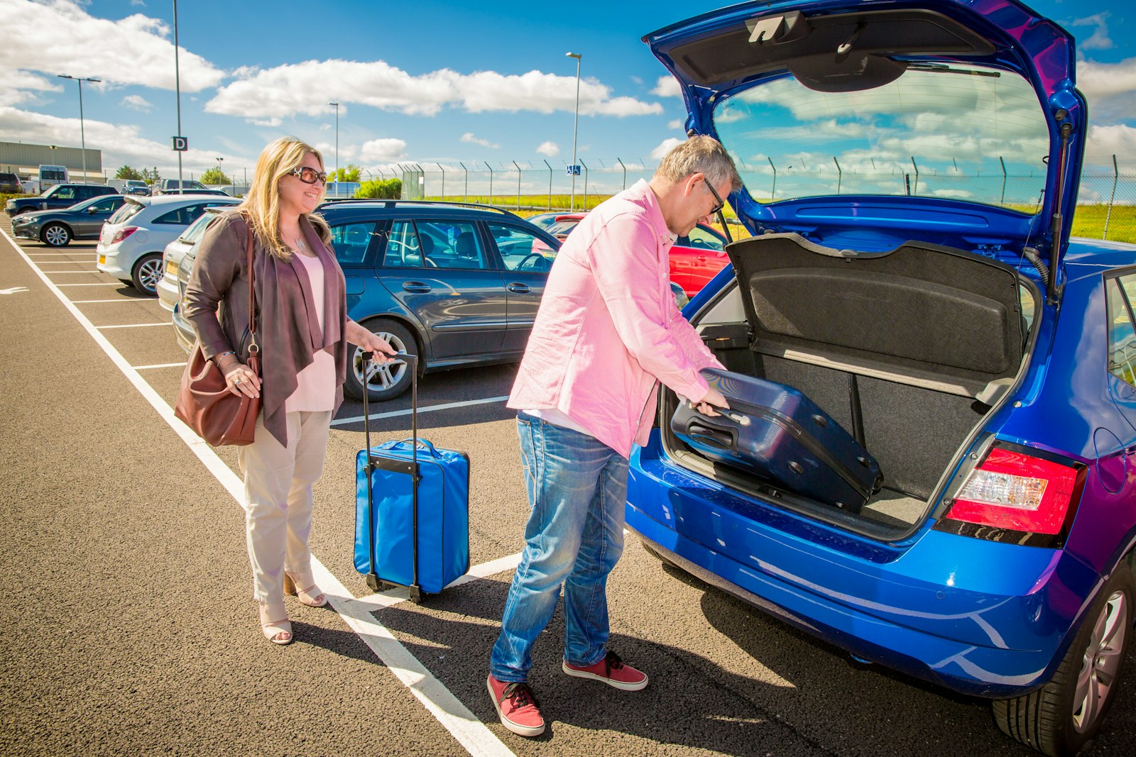 A couple loading a suitcase into the boot of an estate car