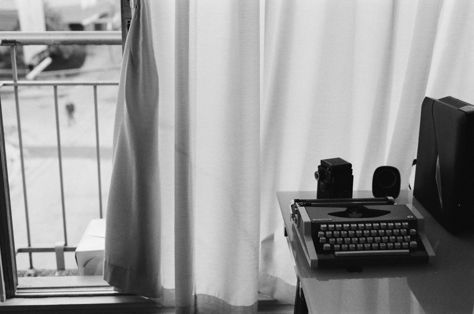 A typewriter and a film camera on a desk beside a curtained window