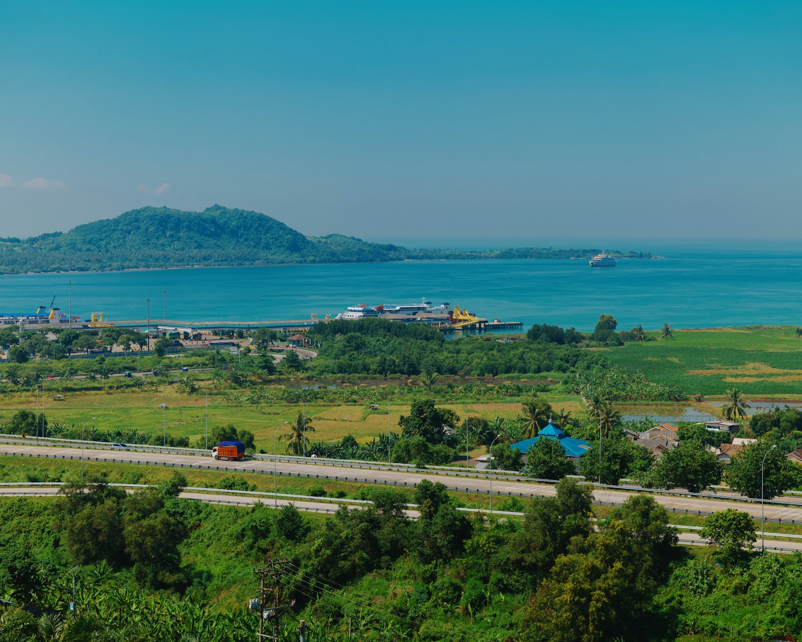 A green island town seen from above with the sea beyond