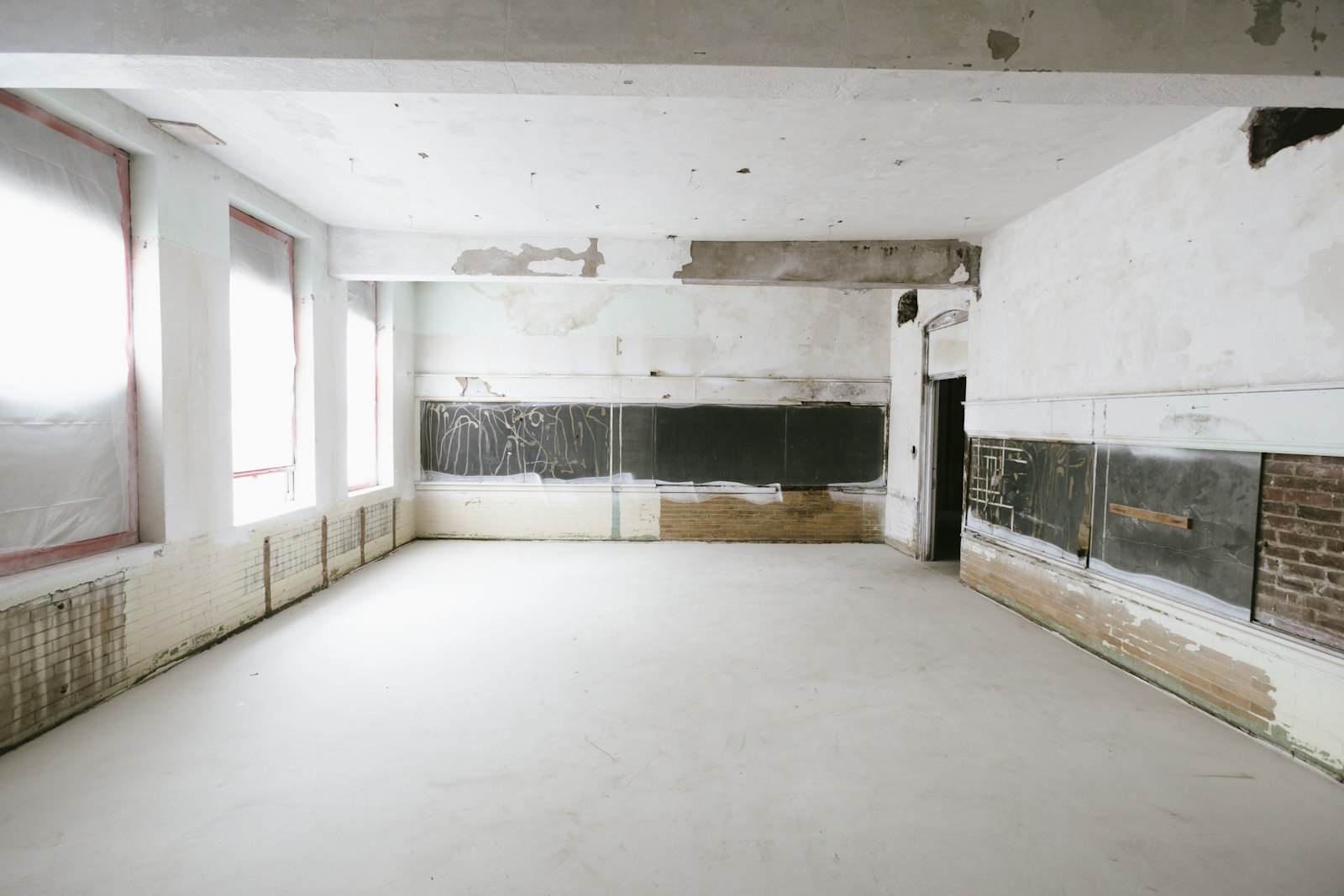 An empty whitewashed room mid-renovation, tall windows letting in daylight
