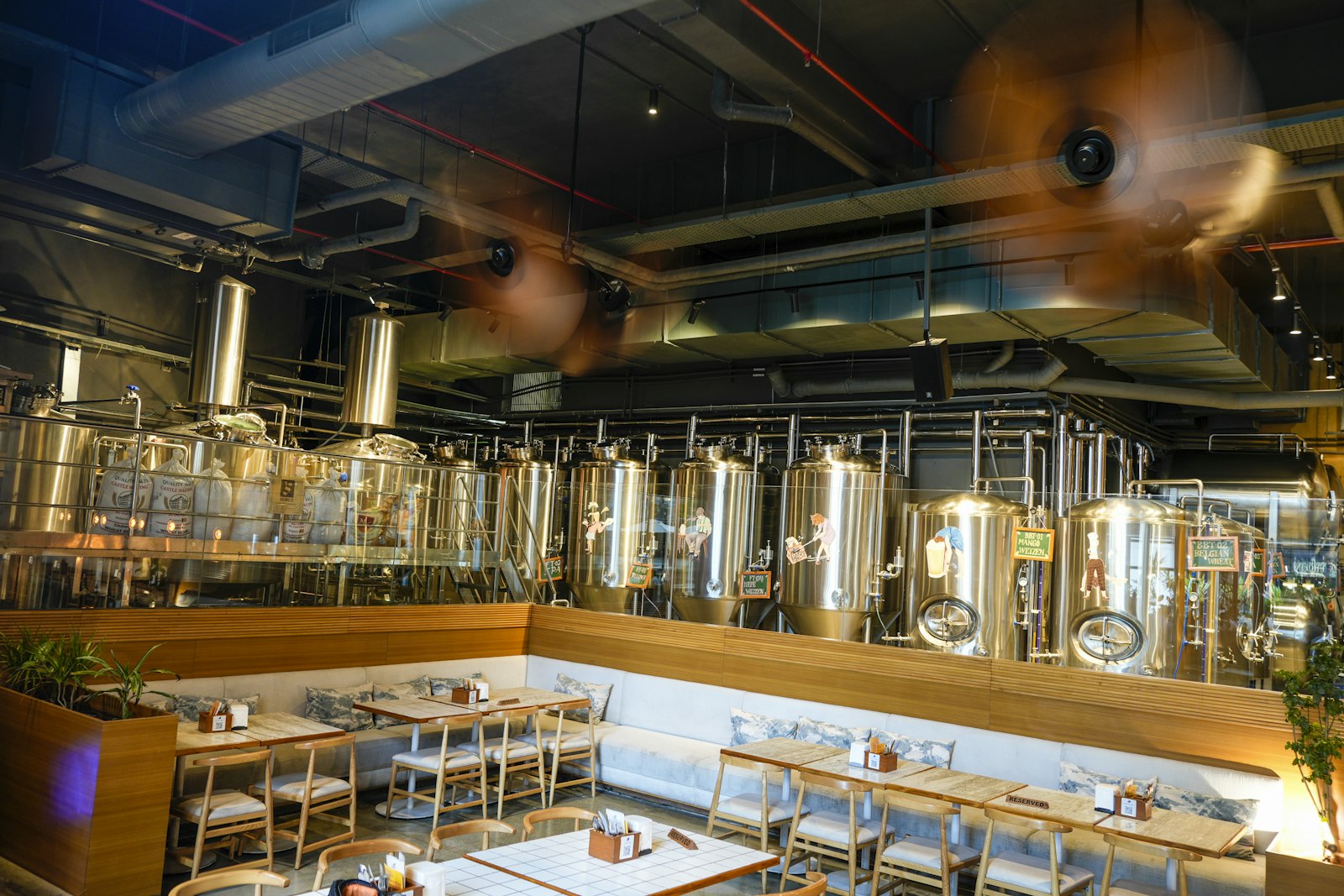 A brewpub dining room with long tables under brewing tanks