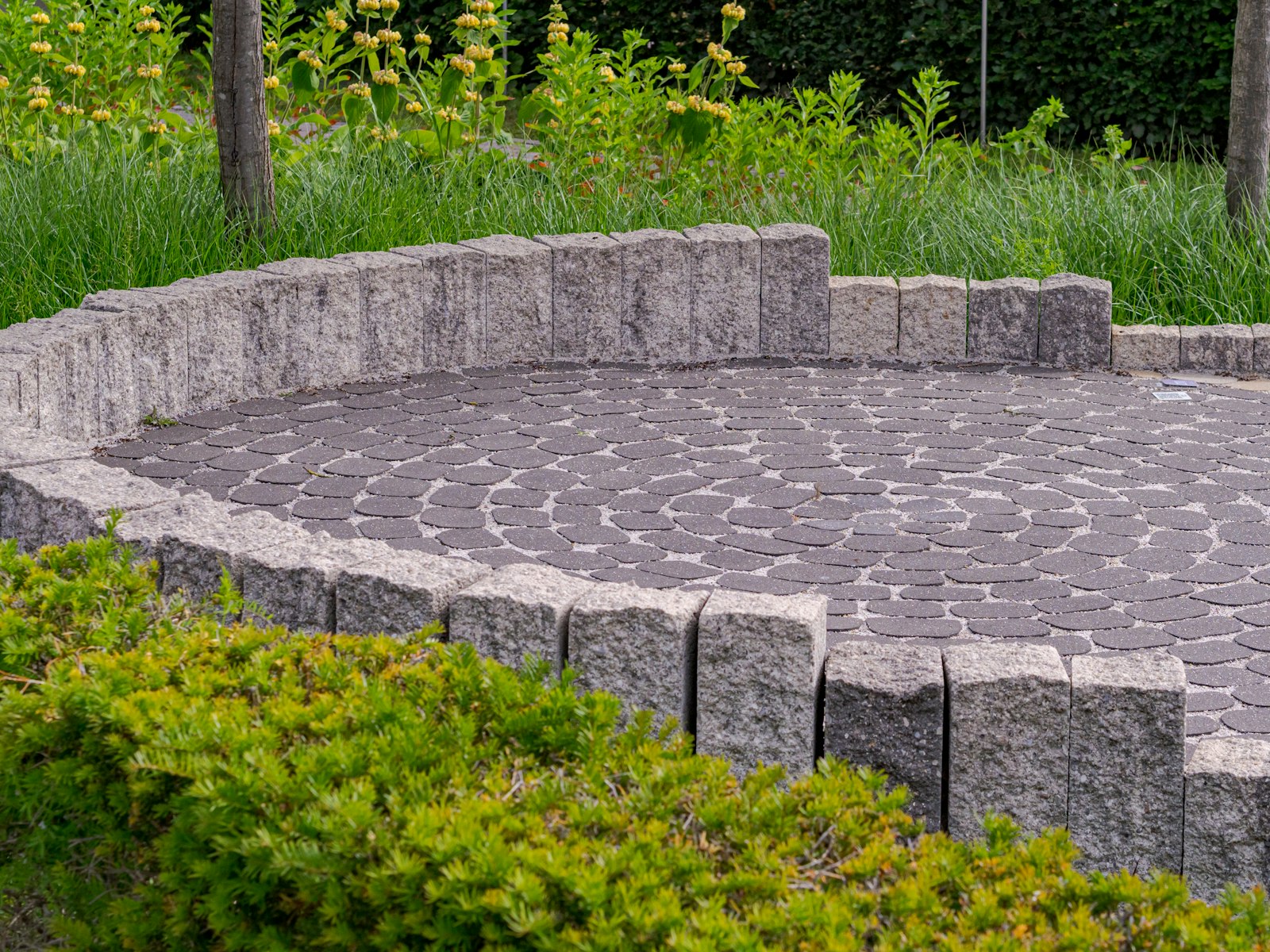 A circular sett patio with a low stone wall and clipped planting around it