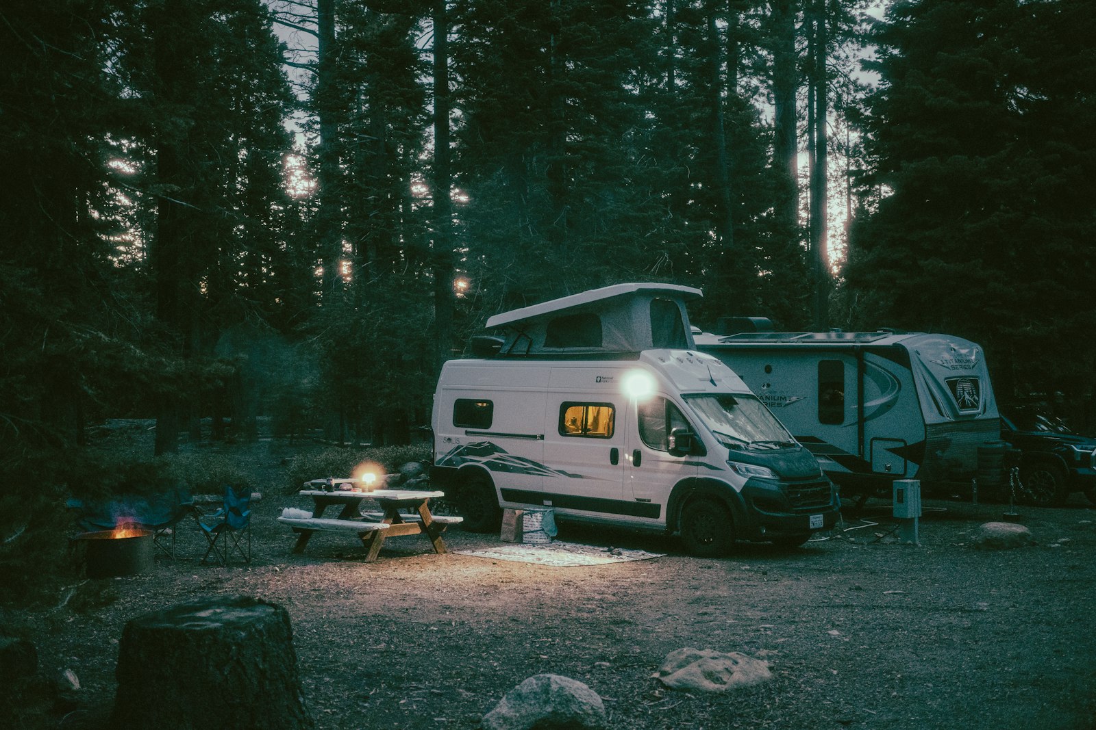 A pop-top camper lit up at a forest campsite at dusk