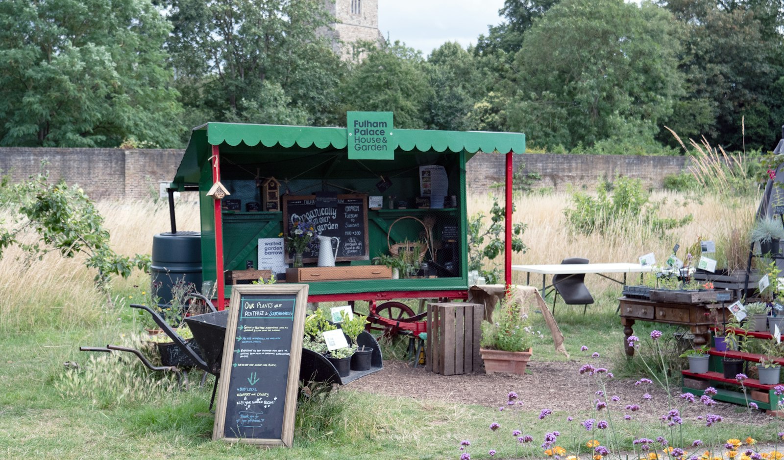 A farm-stall cart with a chalkboard in a meadow by a stone wall