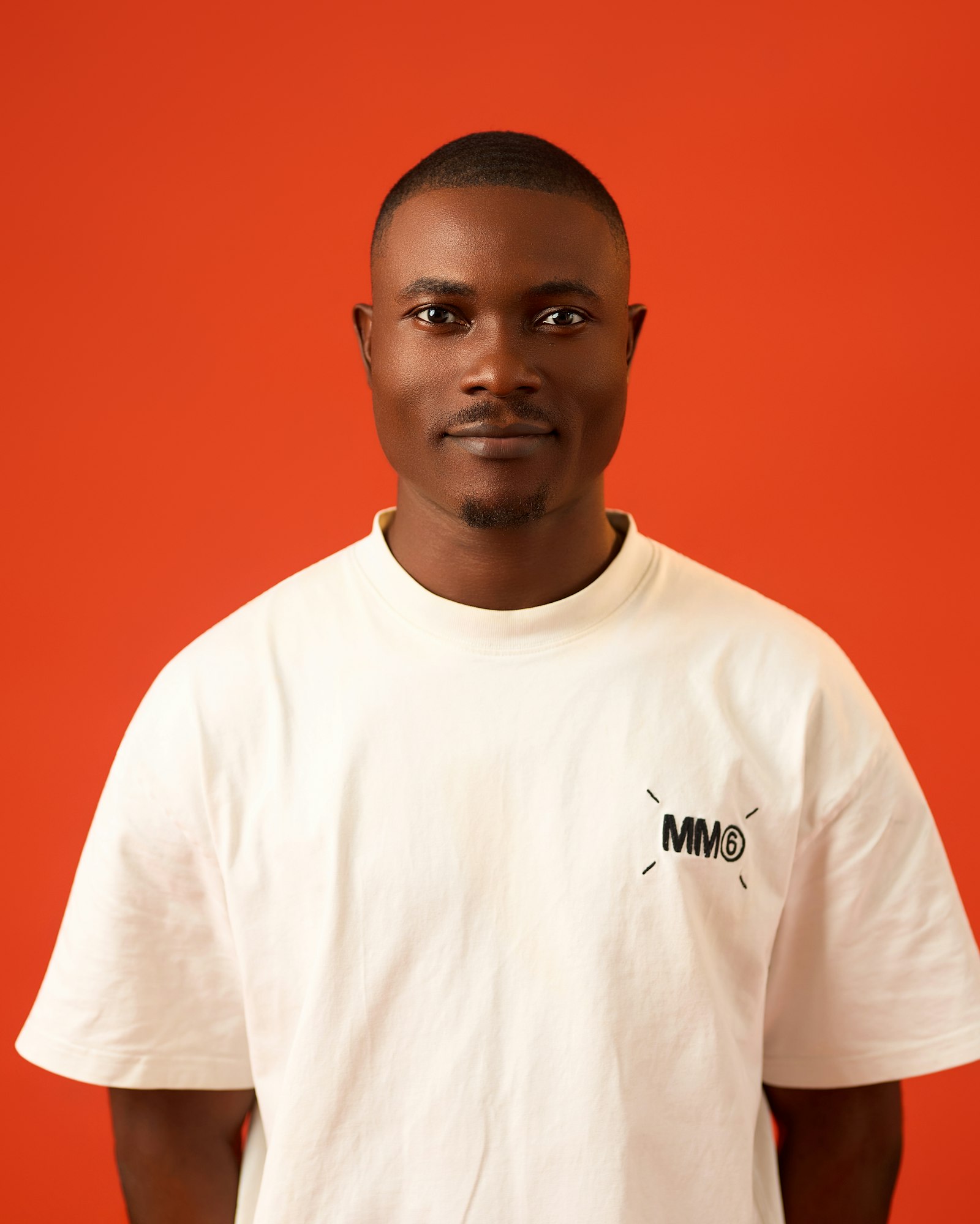 Alex Rivers in a white t-shirt against an orange wall