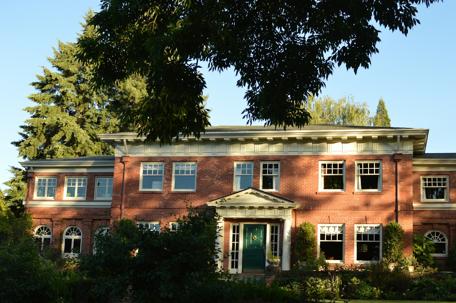 A red-brick Georgian house with a green front door behind trees