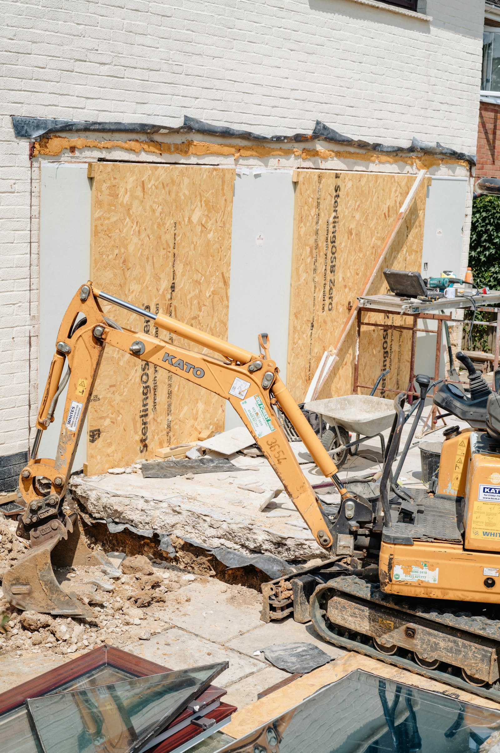 An orange mini digger breaking out a patio beside a house