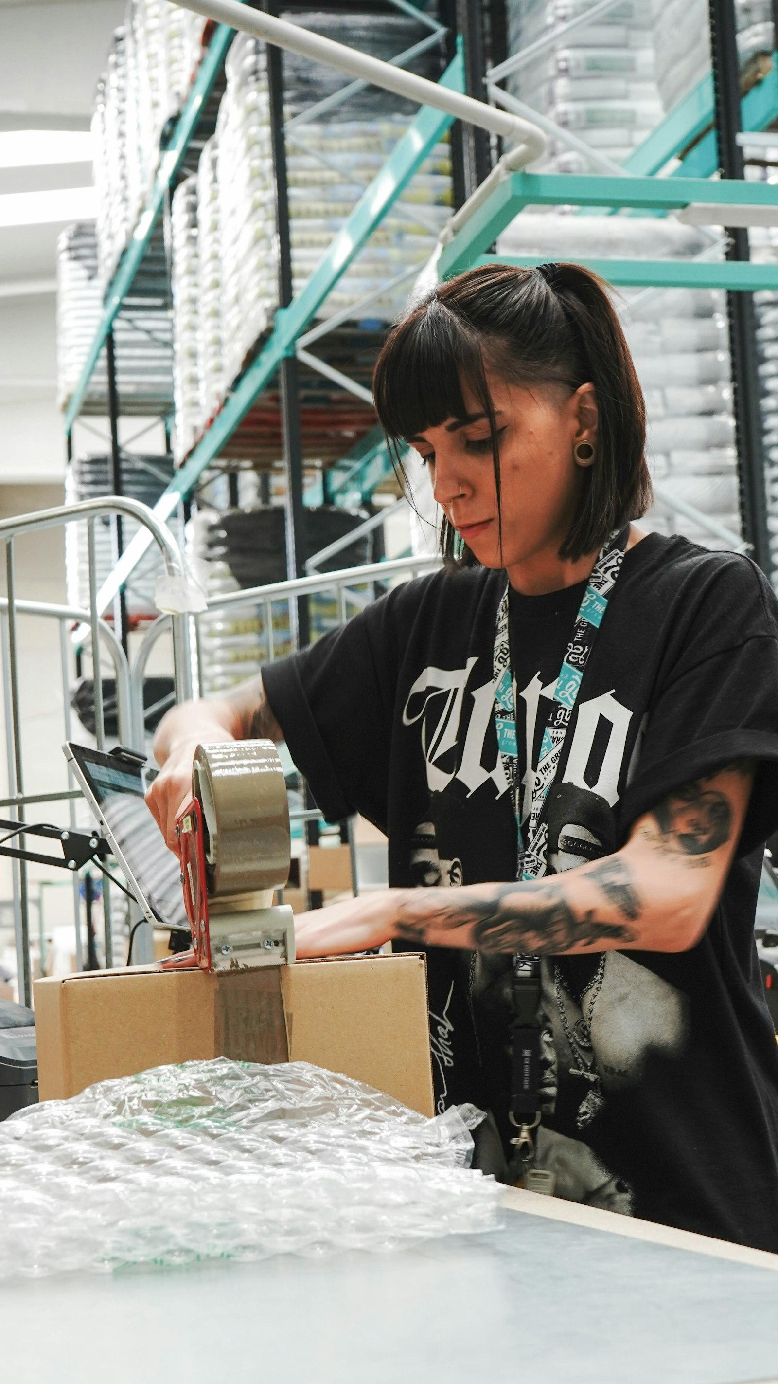 A woman taping a parcel shut with bubble wrap in front and shelving behind
