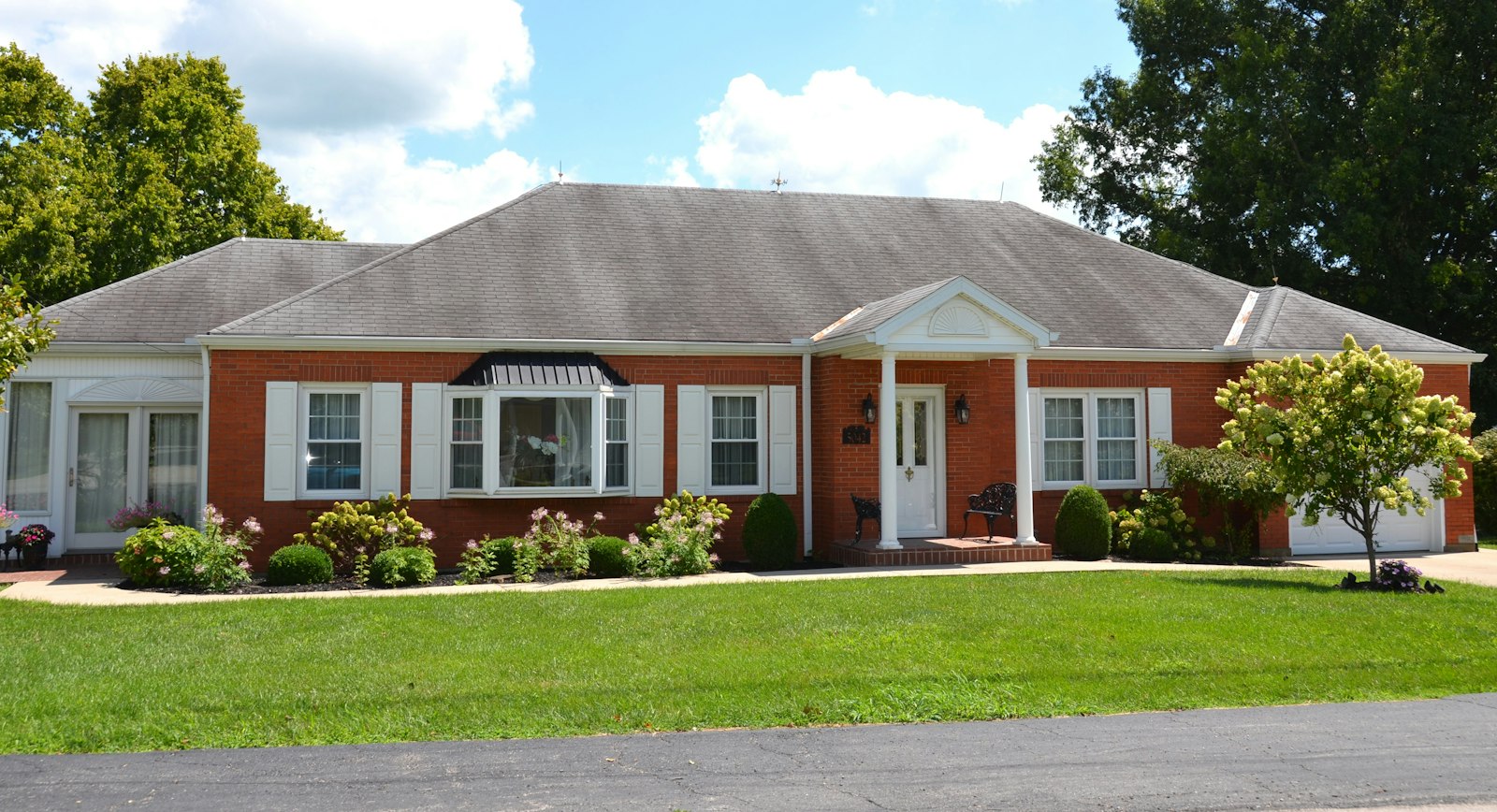 A red-brick bungalow with white shutters and a wide lawn