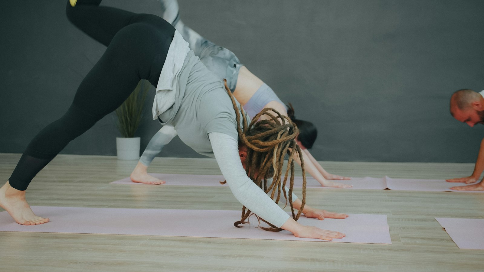 A class in three-legged downward dog on pink mats in front of a painted wall