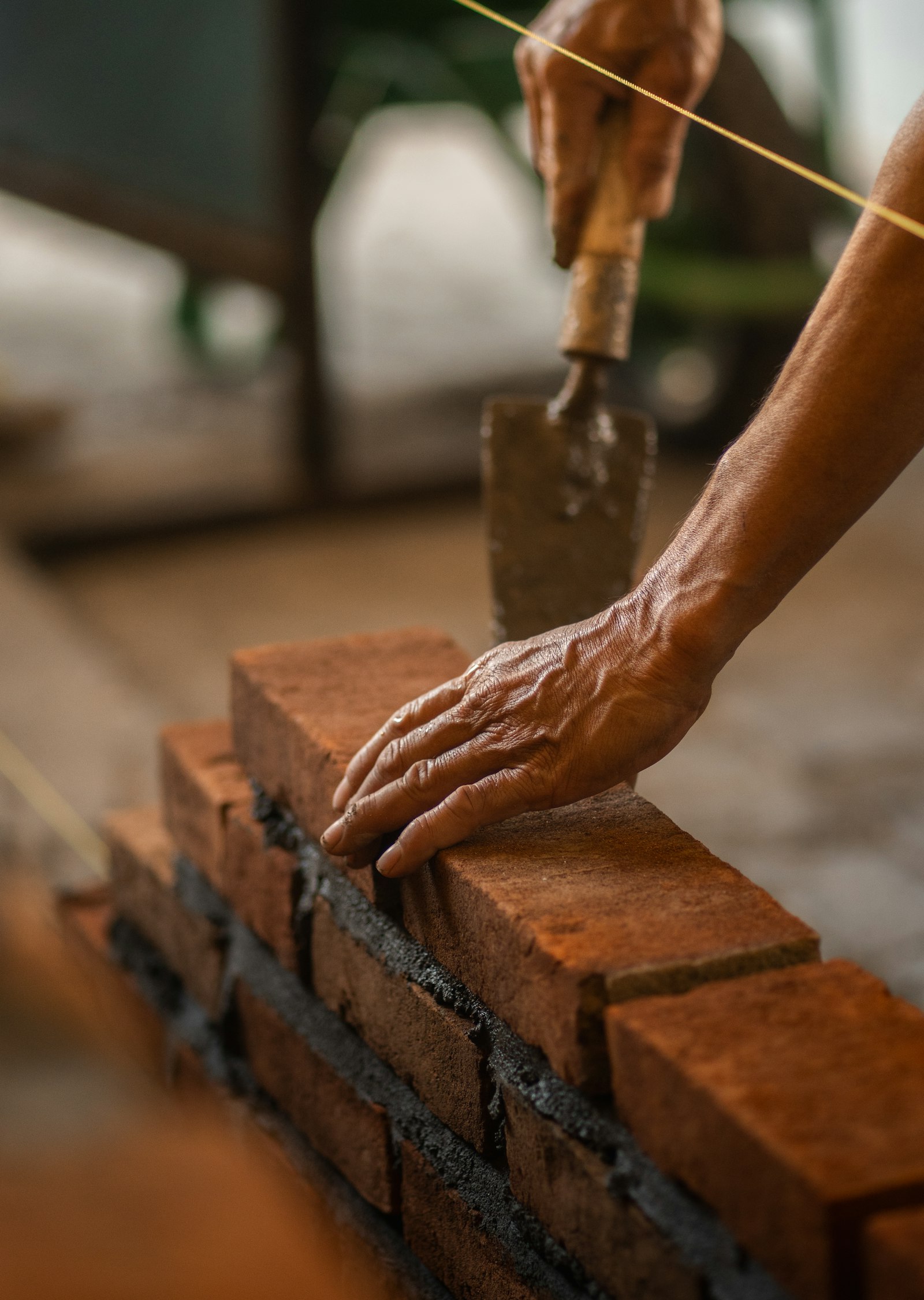 Hands laying a red brick with a trowel and a line