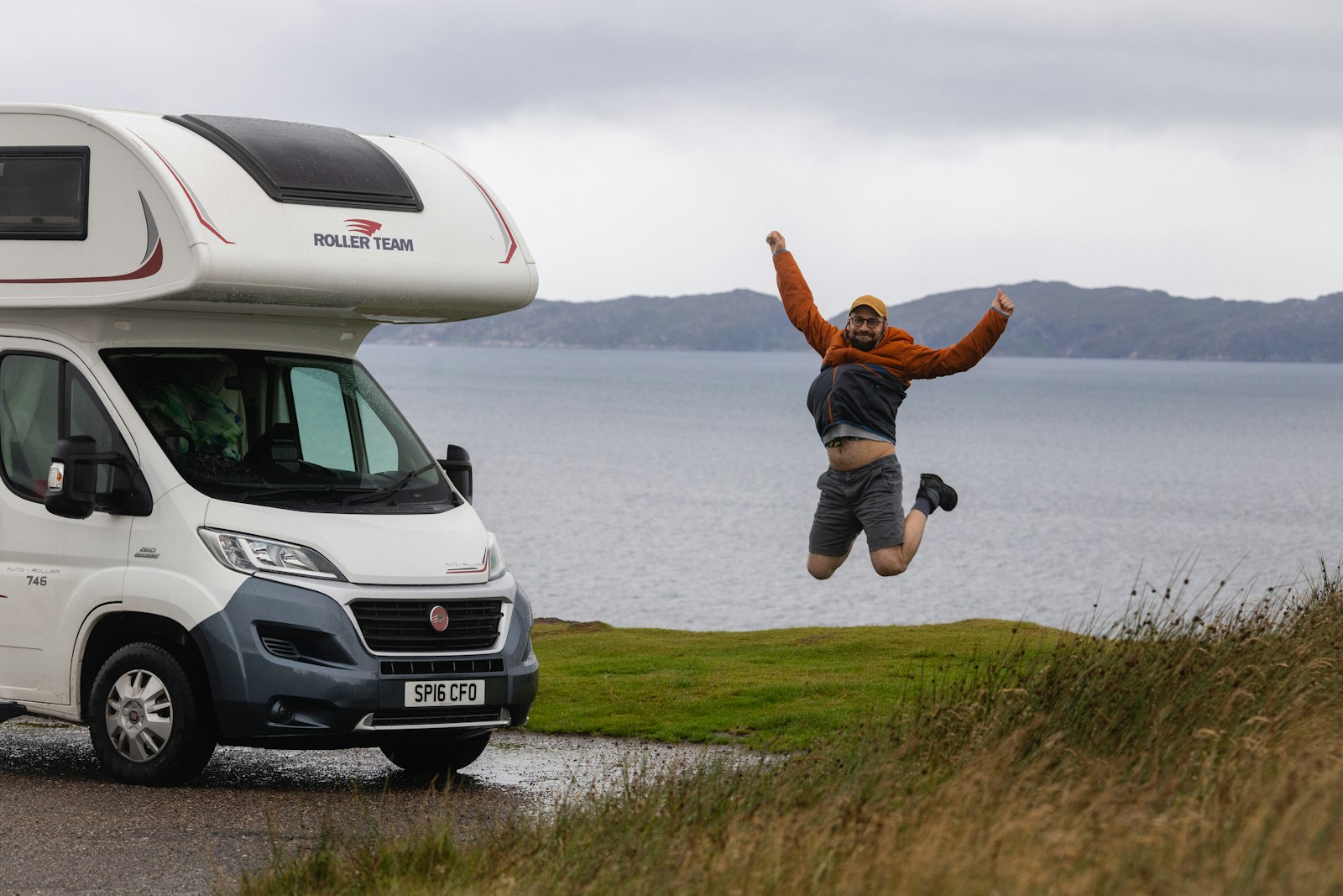 A man jumping for joy beside a motorhome above a loch